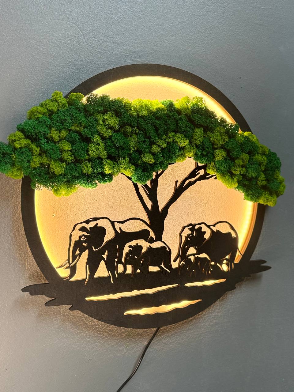 Decorative wall art with silhouettes of elephants and a tree, illuminated from behind.